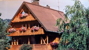 A wooden chalet with a sloped roof, balconies with flower baskets, and a wooden fence. - Apartment 'Hüsli' with Mountain Views, Shared Terrace, and Wi-Fi (Titisee-Neustadt)