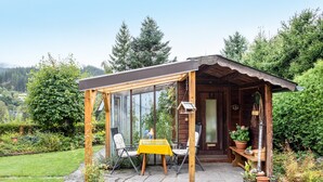A wooden cabin with a covered patio, a table with chairs, and potted plants. - Apartment 'Hüsli' with Mountain Views, Shared Terrace, and Wi-Fi (Titisee-Neustadt)