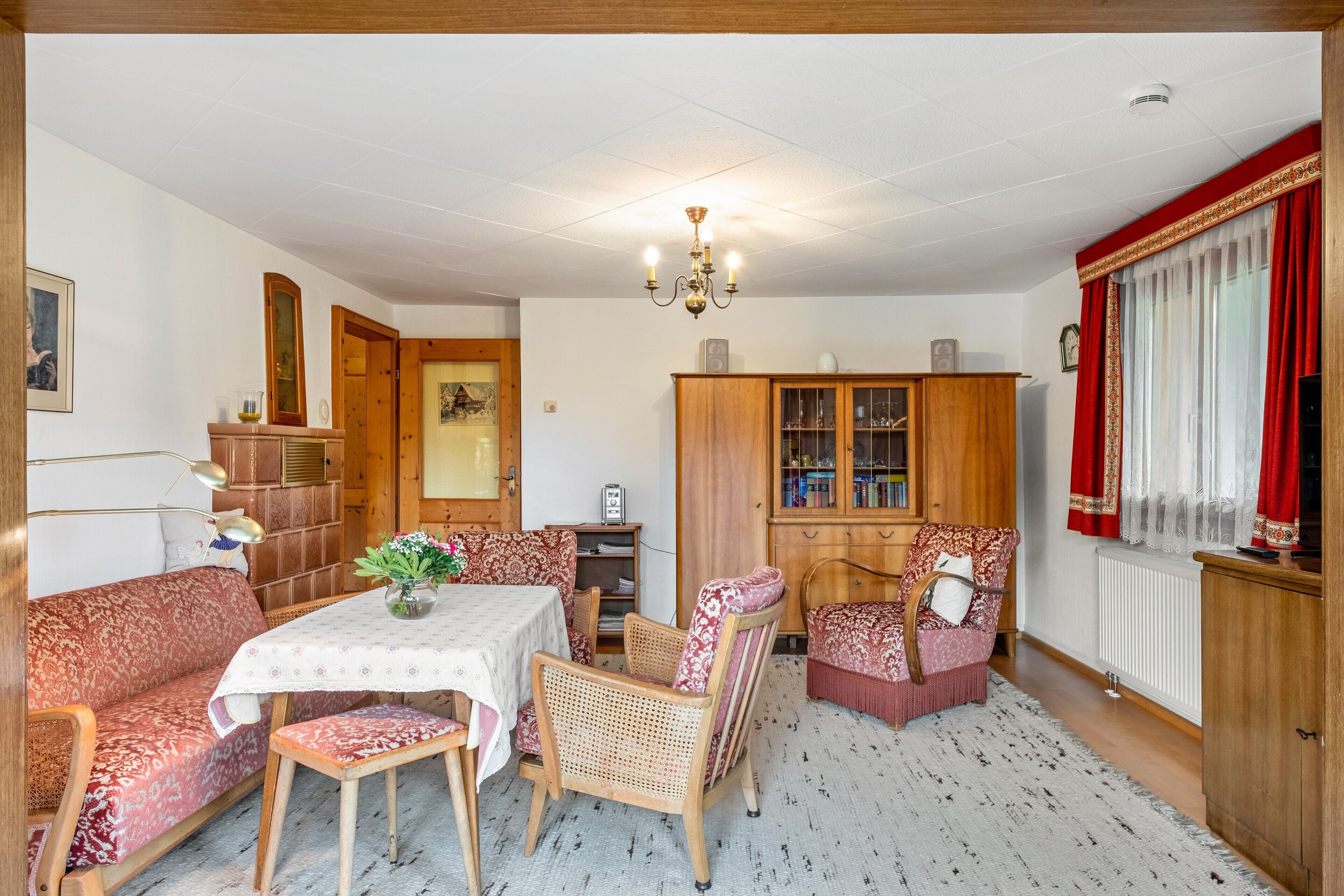 A cozy living room with a dining table, chairs, a sofa, a cabinet, and a chandelier.