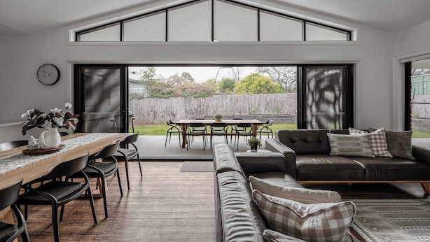 A modern living room with a dining area, large windows, and a view of the backyard. - Luxury On Lakeside (Mount Beauty)