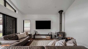 A modern living room with a leather sofa, a flat-screen TV mounted on the wall, and a wood-burning stove. - Luxury On Lakeside (Mount Beauty)