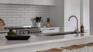 A modern kitchen with a white brick backsplash, stainless steel appliances, and a bar area with stools. - Luxury On Lakeside (Mount Beauty)