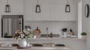 A modern kitchen with white cabinetry, a stainless steel refrigerator, and a dining area with a wooden table and black chairs. - Luxury On Lakeside (Mount Beauty)