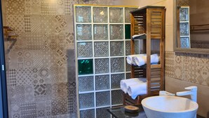 Un baño con un espejo grande, un lavabo redondo y una ducha con puerta de cristal.