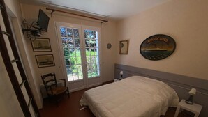 A bedroom with a bed, a chair, a desk, a TV, and a window with a view of greenery. - House for rent in Oléron (La Rémigeasse) 100 m from the beach (6 people) (Dolus-d'Oléron)