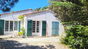 A two-story building with a white exterior and green shutters, surrounded by greenery and a gravel path. - House for rent in Oléron (La Rémigeasse) 100 m from the beach (6 people) (Dolus-d'Oléron)