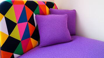 Een hoek van een kamer met een kleurrijk hoofdeinde met een geometrisch patroon en twee paarse kussens.