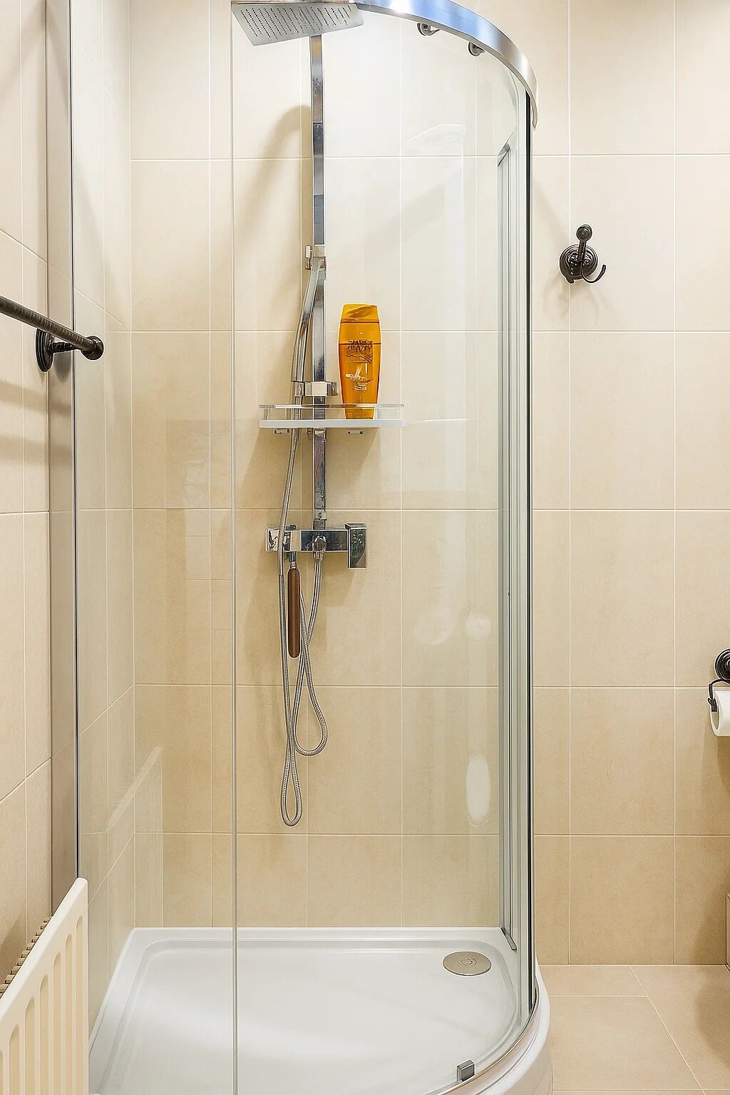 Een douchecabine met glazen wanden, een handdouche, een zeepdispenser en een handdoekrek.