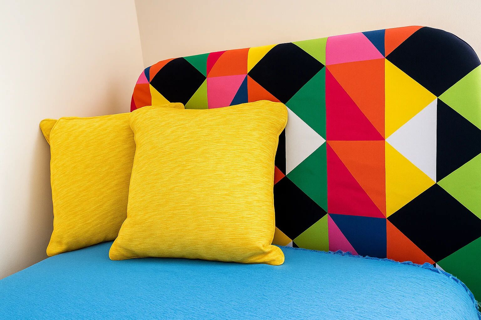 A bed with a blue mattress and two yellow pillows against a headboard with a colorful geometric pattern.