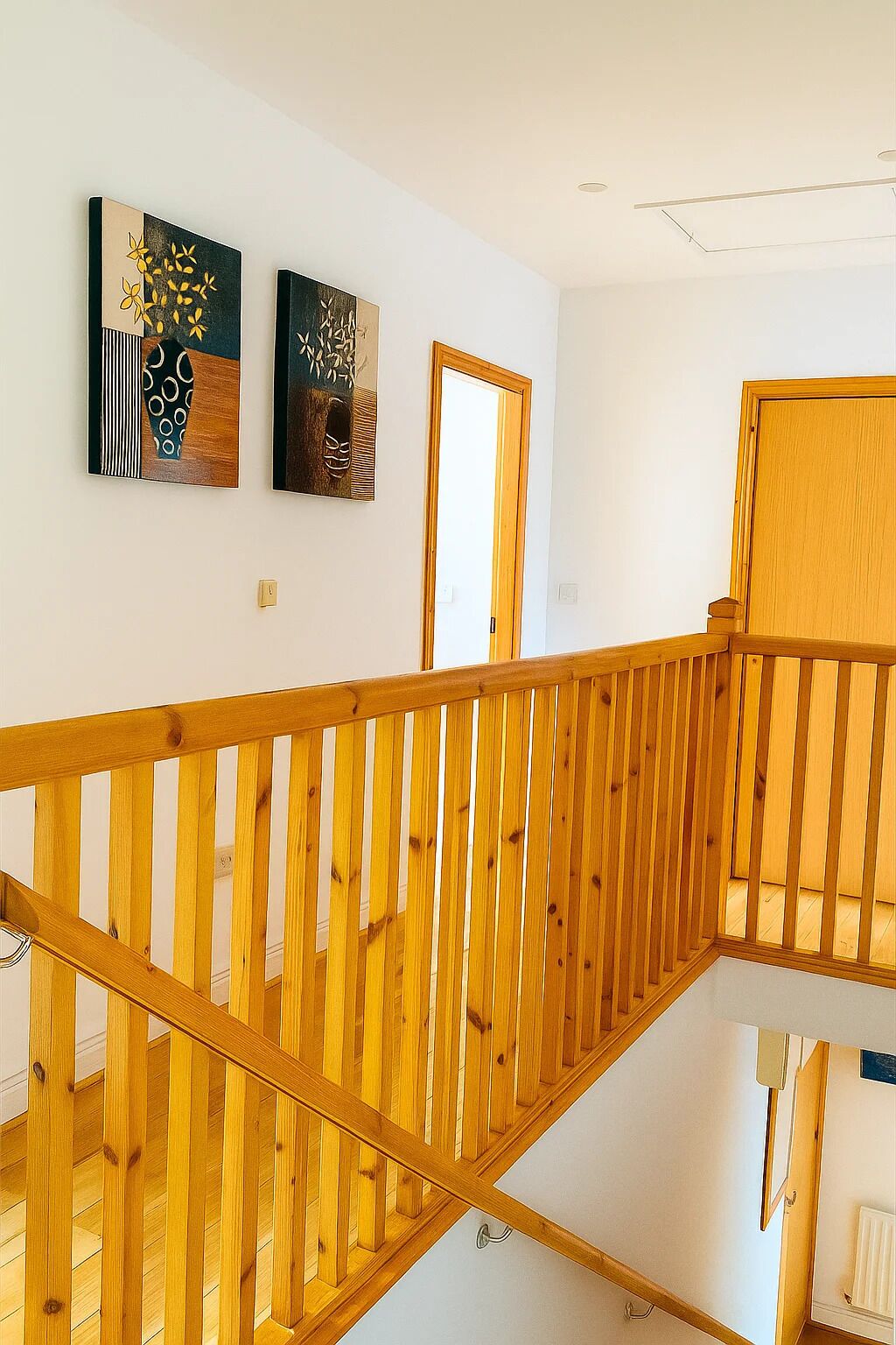 A wooden staircase with a railing, white walls, and two artworks above the door.