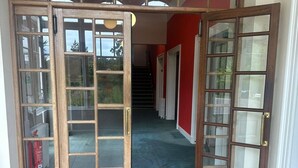 A set of wooden French doors with glass panels leading to a hallway with a red wall and a staircase. - Cluny Hill Hotel (Forres)