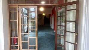 A hallway with a black mat, wooden doors with glass panels, and a staircase in the background. - Cluny Hill Hotel (Forres)