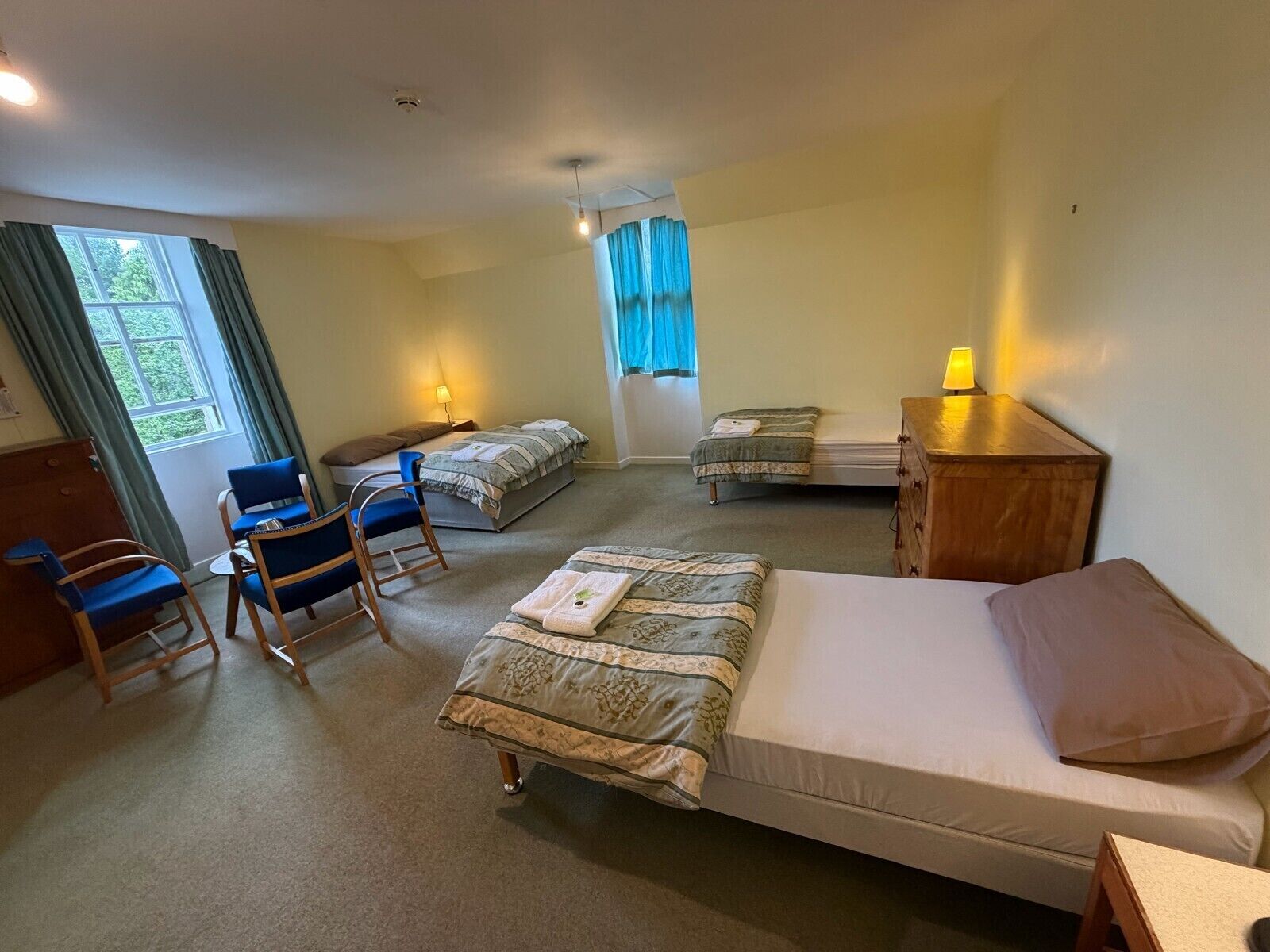 A hotel room with a single bed, a desk, a chair, a small table, and a window with curtains.