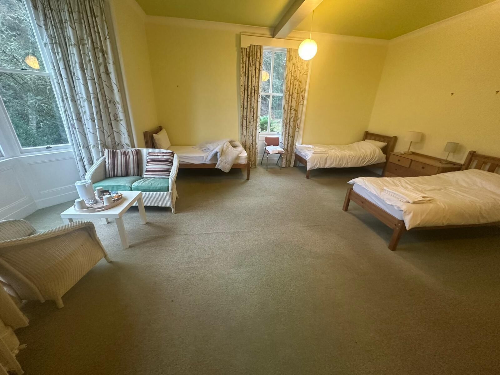 Une chambre d’hôtel avec un canapé, deux lits simples, une petite table avec un plateau, et une fenêtre avec des rideaux.