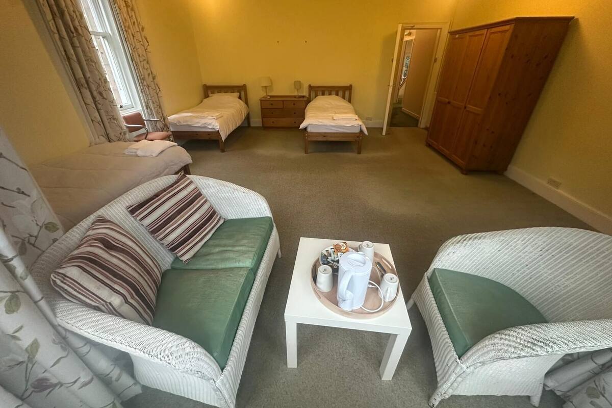 A room with two beds, a sofa, a small table with toiletries, and a wardrobe.