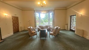 A spacious room with a high ceiling, a chandelier, a large window with curtains, and a seating area with chairs and a table. - Cluny Hill Hotel (Forres)