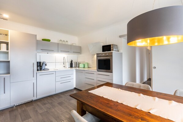 A modern kitchen with white cabinetry, a wooden dining table, and a large overhead light fixture.