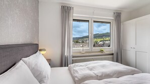 A bedroom with a bed, a window with curtains, a radiator, and a view of a landscape. - Apartment '7' with Shared Garden and Wi-Fi (Willingen (Upland))