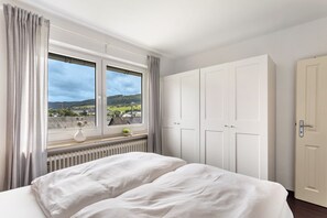 Une chambre avec une grande fenêtre, un lit, une armoire et un radiateur.