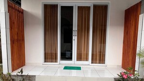 A modern entrance with a set of steps leading to a glass door, flanked by wooden panels and potted plants. - Ajik Guest House (Ubud)