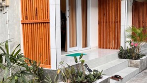 A modern building with a covered entrance, wooden sliding doors, and a concrete staircase leading to the entrance. - Ajik Guest House (Ubud)
