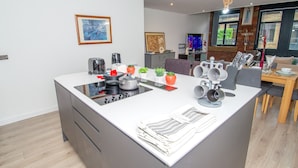 A modern kitchen with a central island, built-in appliances, and a dining area with a wooden table and chairs. - New Apartment - Sleeps 4 - Parking - City Centre (Bradford)