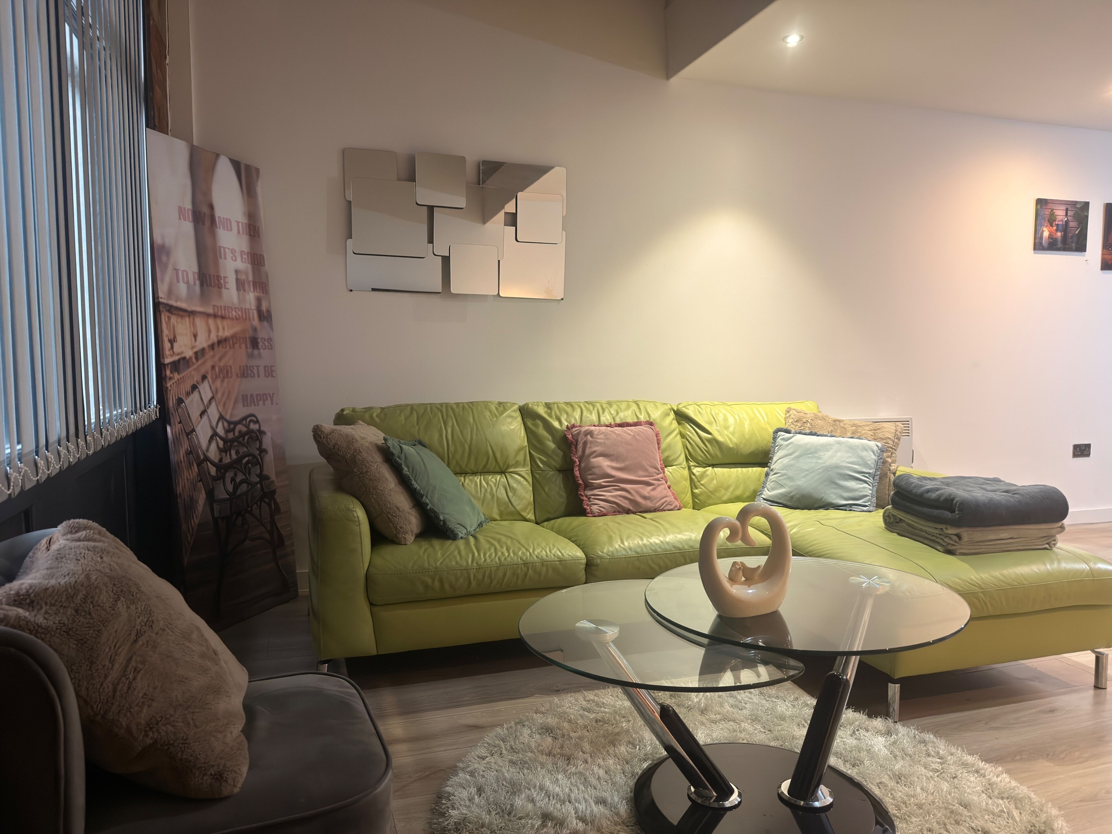 Ein modernes Wohnzimmer mit einem grünen Ledersofa, einem Glastisch und einem flauschigen Teppich.