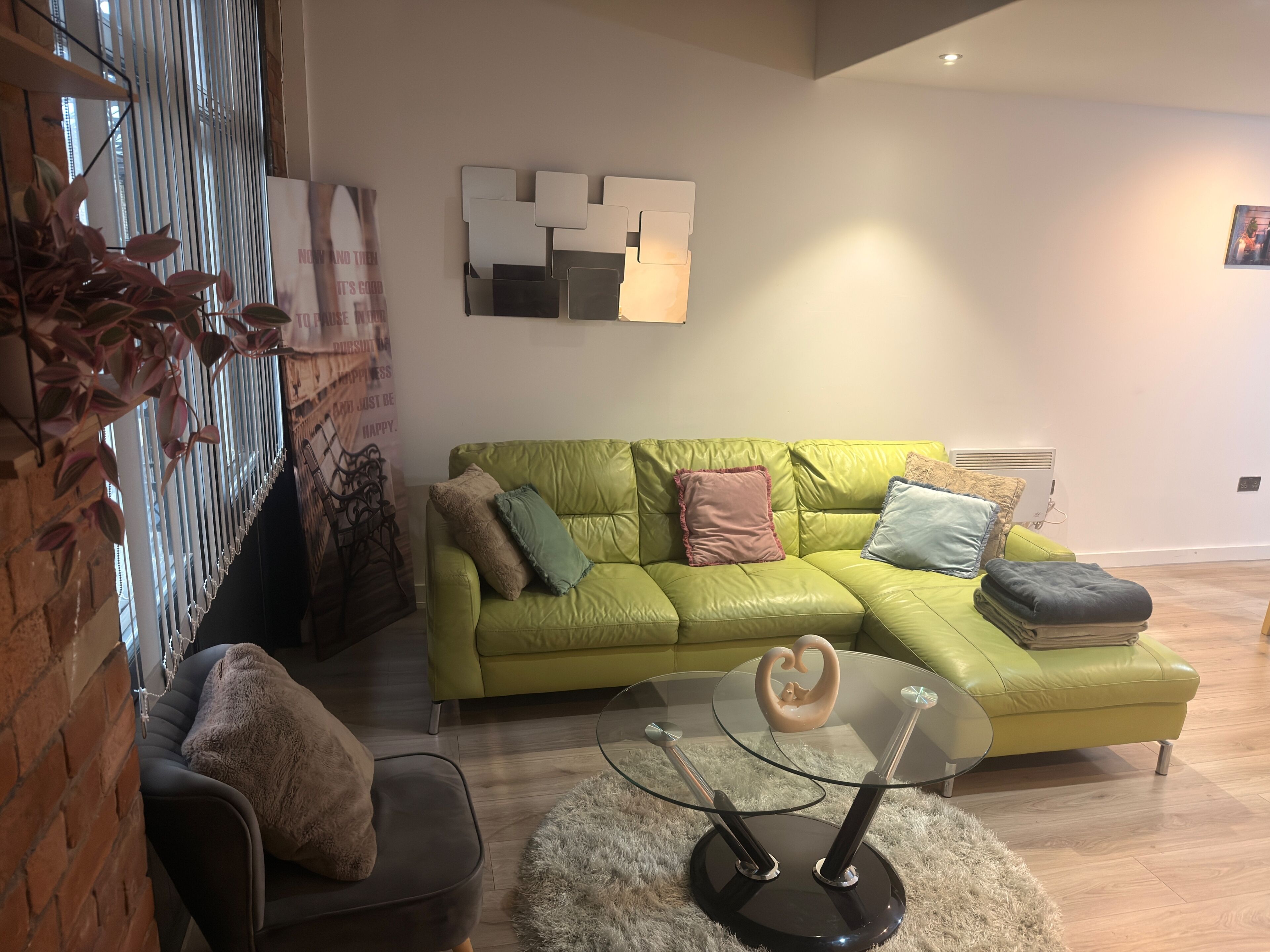 A modern living room with a green leather sofa, a glass coffee table, and a decorative wall piece.