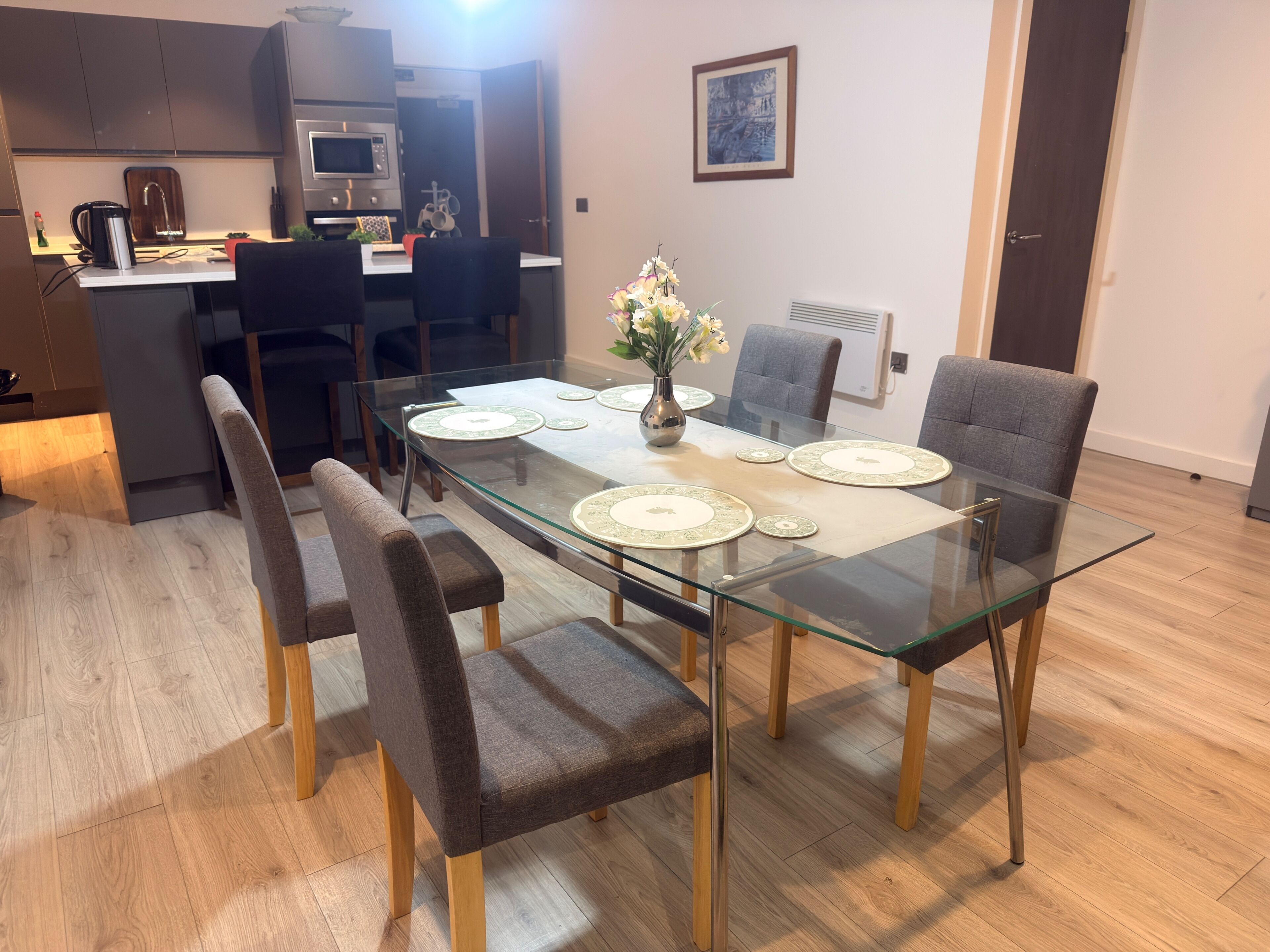 A modern dining area with a glass table, four chairs, and a vase with flowers.