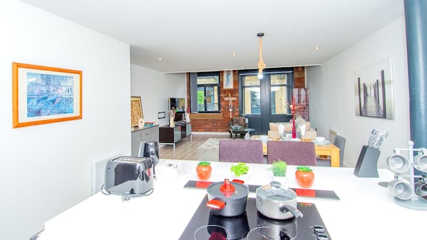 A modern kitchen with a dining area, featuring a central island with a stove, a dining table with chairs, and a view into the living room. - New Apartment - Sleeps 4 - Parking - City Centre (Bradford)