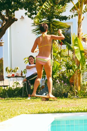 Une personne en bikini, debout près d’une piscine, avec une table et des chaises à proximité.