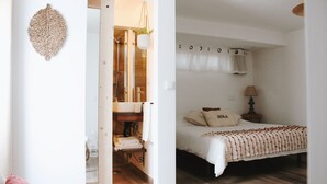 A bedroom with a bed, a nightstand, a lamp, and a bathroom visible through an open door.