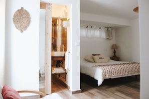 A bedroom with a bed, a nightstand, a lamp, and a bathroom visible through an open door.