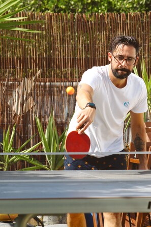 Une personne joue au ping-pong à l’extérieur, avec une clôture en bambou en arrière-plan.