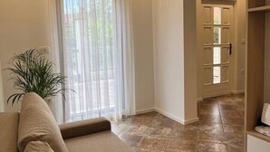 A living room with a beige sofa, a potted plant, and a sliding glass door leading to a tiled hallway. - Lovely 2-bedroom apartment with terrace & parking (Izola)