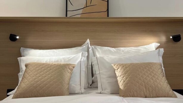 A neatly made bed with white and beige pillows, a wooden headboard, and two wall-mounted night lights. - Lovely 2-bedroom apartment with terrace & parking (Izola)