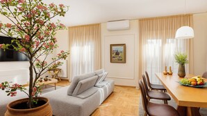 Una sala de estar con sofá, una mesa de comedor con sillas, una planta en maceta y un cuadro en la pared.
