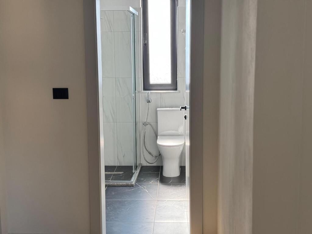 A bathroom with a toilet, a shower, and a small window.