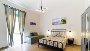 Un dormitorio con cama, mesitas de noche, una reposera, lámpara colgante y un cuadro en la pared.