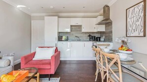 Eine moderne Küche mit weißen Schränken, einem roten Sofa und einem Essbereich mit Holzsesseln.
