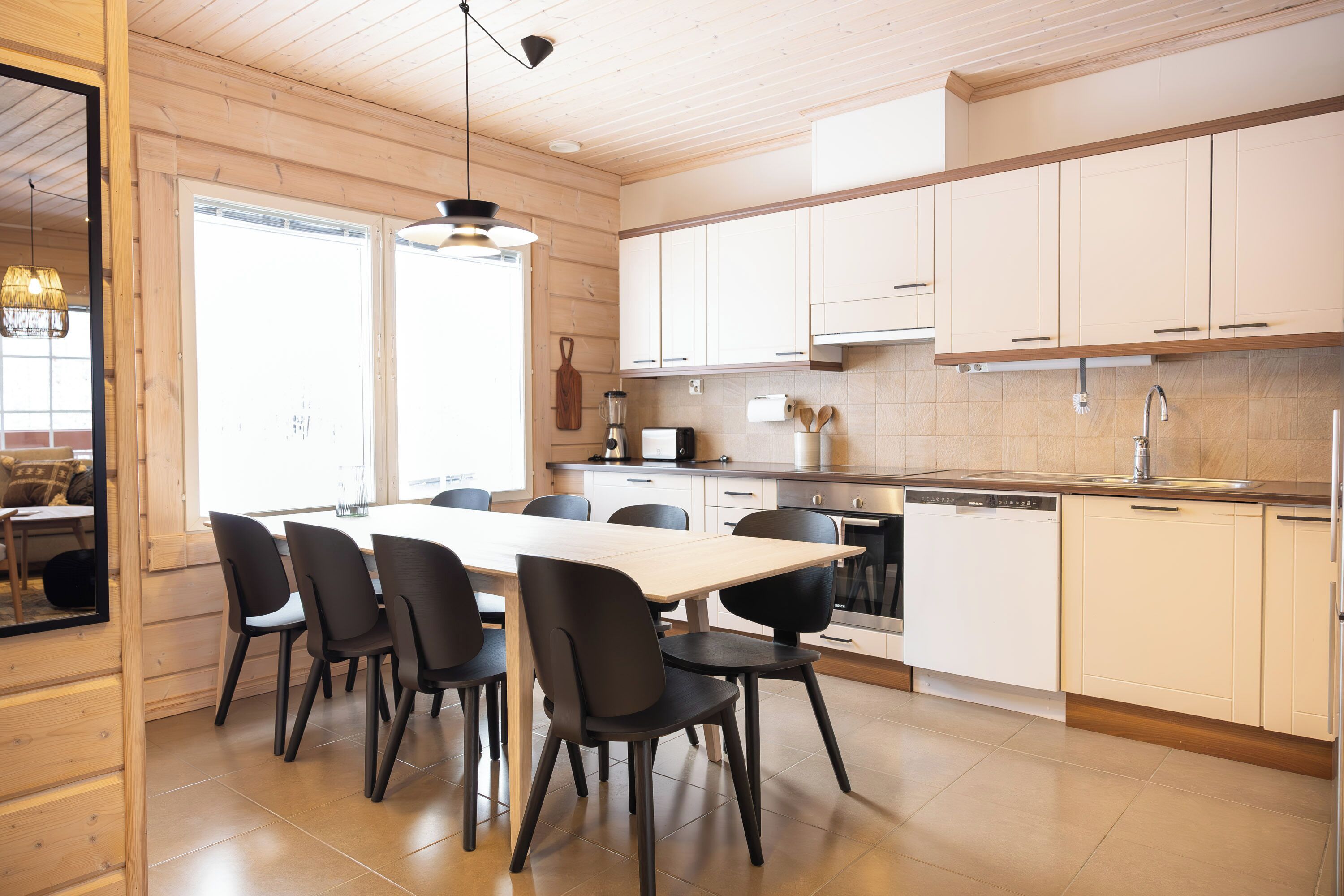 A modern kitchen with wooden cabinets, a dining table with chairs, and a large window providing natural light.