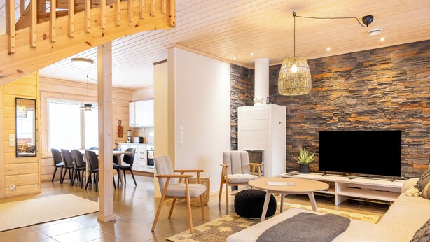 A modern living room with a stone wall, a flat-screen TV, and a wooden ceiling. - Villa Pyry (Sotkamo)