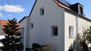 Una casa moderna de dos pisos, con techo inclinado, ventanas pequeñas y una chimenea visible.