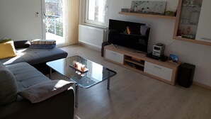 Una sala de estar moderna con un sofá, una mesa de centro de vidrio, un televisor y una estantería.
