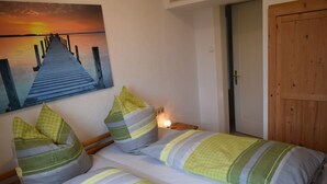 Una habitación con una cama, almohadas, un cuadro de una puesta de sol sobre un muelle y una puerta de madera.