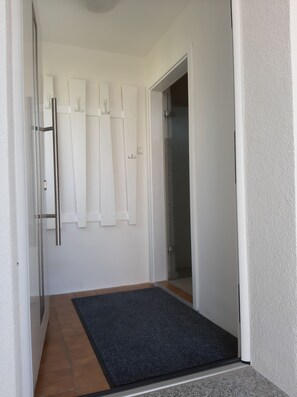 Un passadís amb un estri de peu fosc a l'entrada, parets blanques i una porta que dona a una habitació.