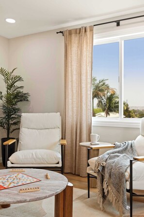 A modern living room with a white armchair, a round coffee table, and a view of palm trees through a window.