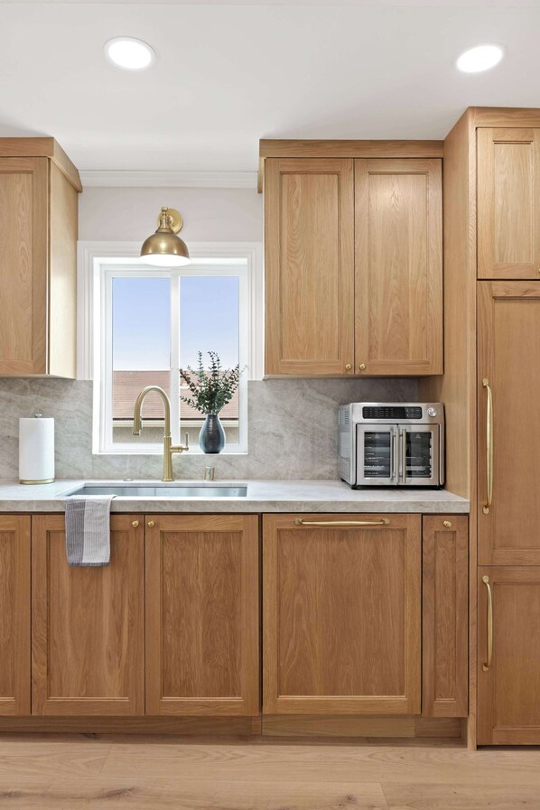 A kitchen with wooden cabinets, a stainless steel sink, a built-in oven, and a window above the sink.