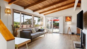 A modern living room with a wooden ceiling, a sofa, a TV, and a large window. - Casual La Jolla Gem , Views & Space for 10 (San Diego)