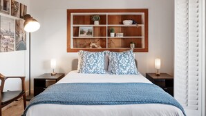 A neatly arranged bedroom with a large bed, two bedside tables with lamps, a wall-mounted shelf with decorative items, and a chair. - Casual La Jolla Gem , Views & Space for 10 (San Diego)